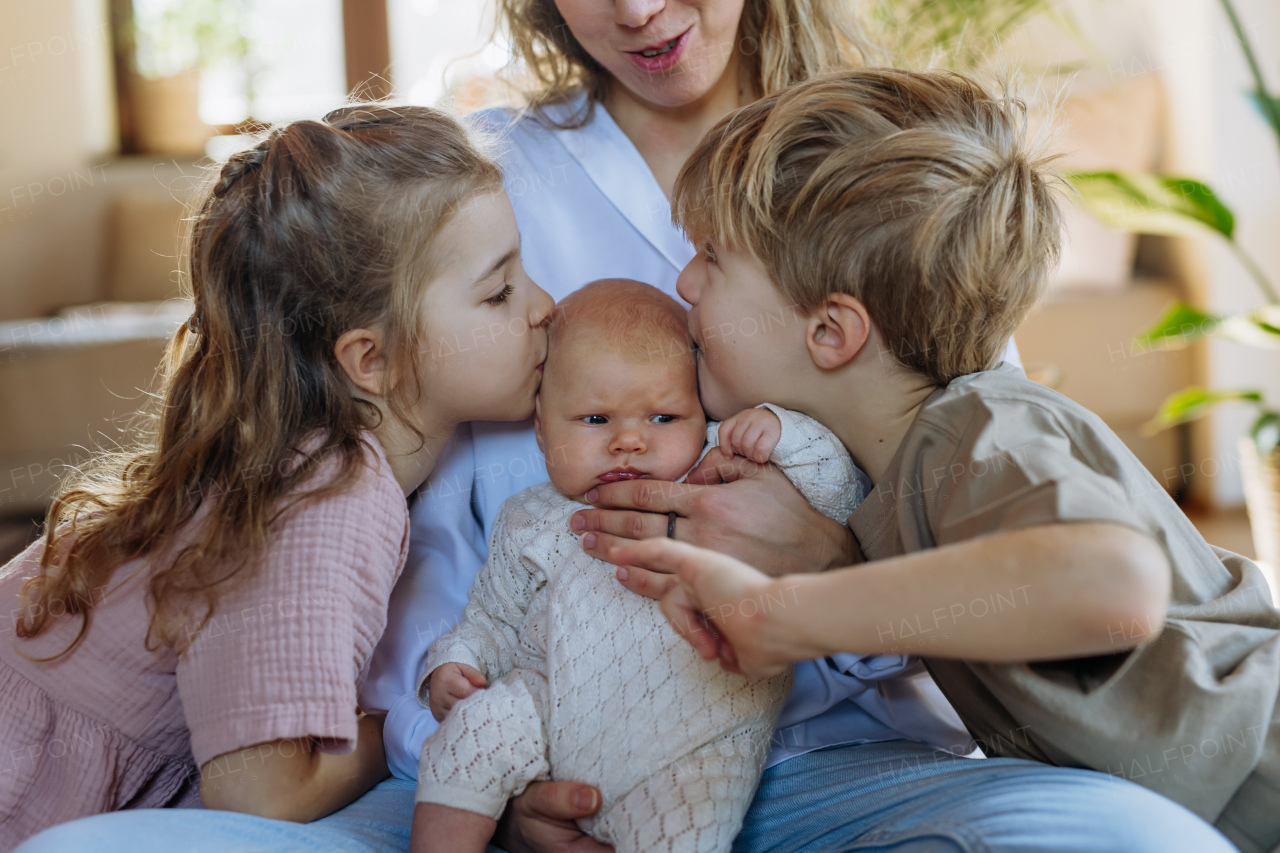 Siblings kissing the cheeks of a little baby. Big brother and big sister meeting newborn sister, enjoying together time. Family bonding.