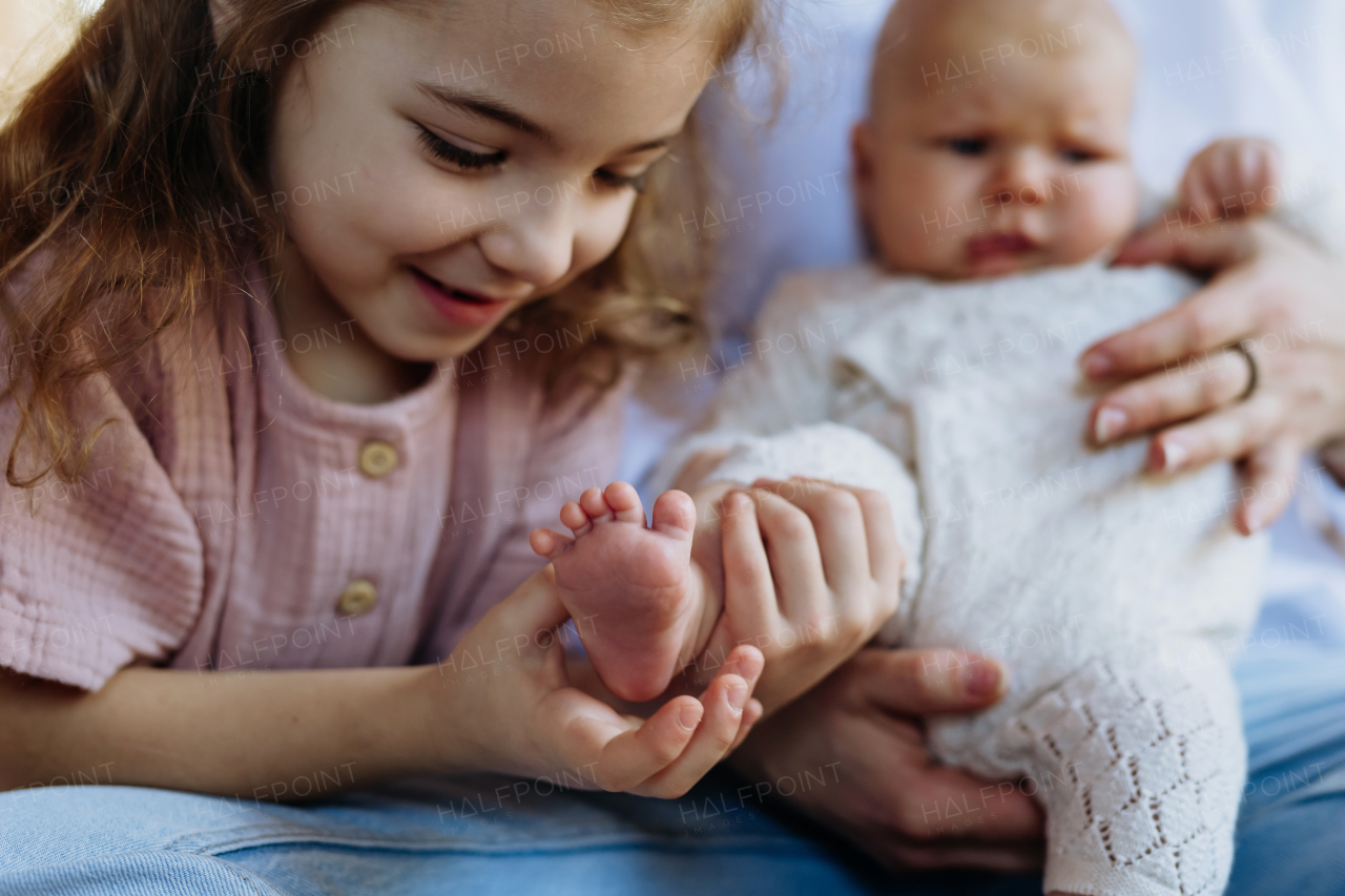 Portrait of big sister kooking at small foot of little baby, smiling. Sisterly love, joy for new family member.