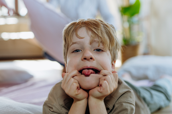 Portrait of boy with easter bunny ears on head, boy lying on belly, making faces, grimace.