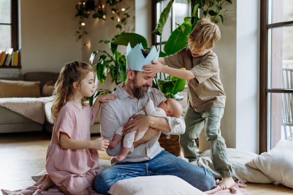 Father with paper crown on head holding newborn baby, enjoying all his kids. New sibling. Unconditional paternal love and Father's Day concept.