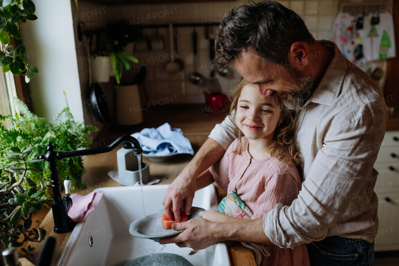 Dad and cute daughter washing dishes in sink together. Girls dad. Unconditional paternal love, Father's Day concept.