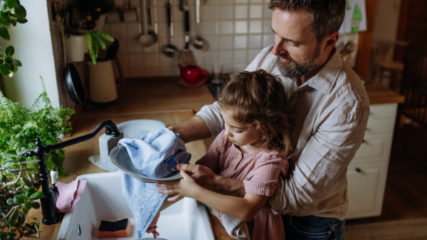 Dad and daughter drying dishes with towels, after washing them together. Girls dad. Unconditional paternal love and Father's Day concept.