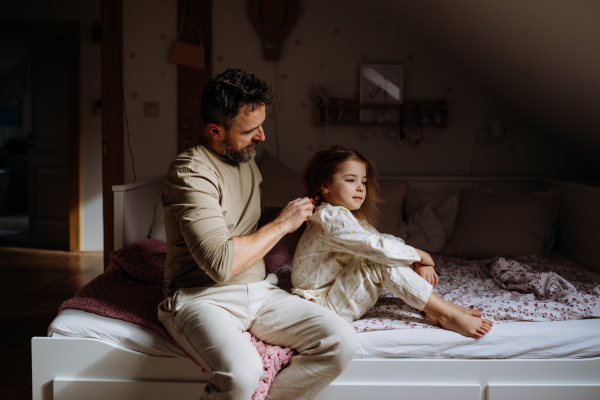 Father braiding his daughter's hair, combing hair as part of bedtime routine. Single dad taking care of his daughter's hairstyle.