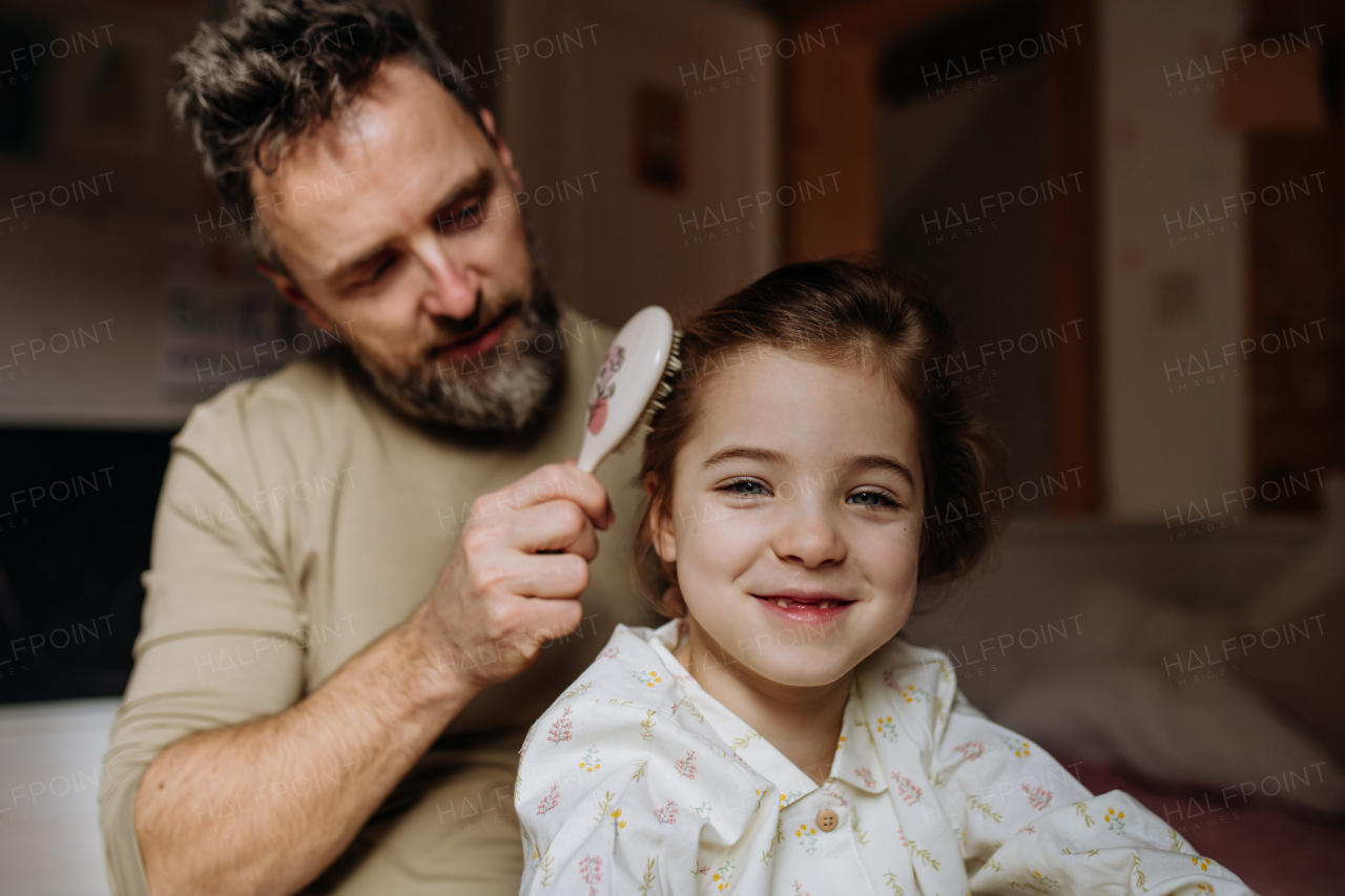 Father braiding his daughter's hair, combing hair as part of bedtime routine. Single dad taking care of his daughter's hairstyle.