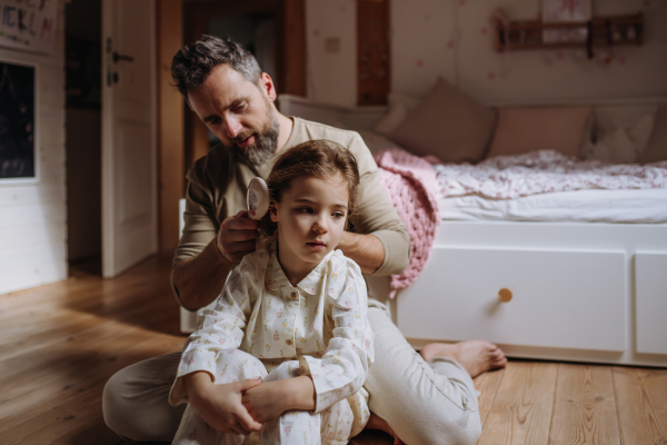 Father braiding his daughter's hair, combing hair as part of bedtime routine. Single dad taking care of his daughter's hairstyle.