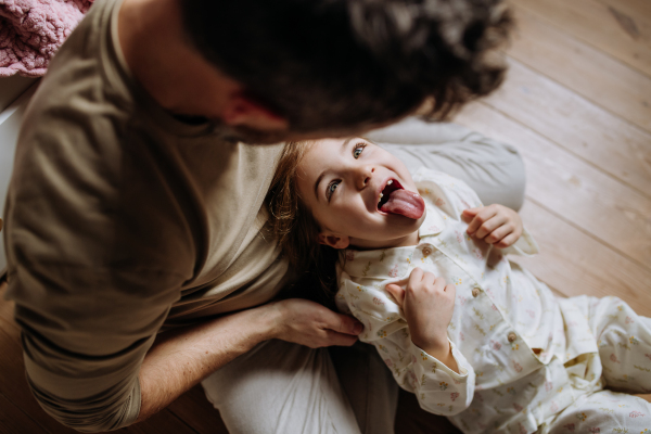 Top view of father with daughter on floor laughing together, having fun and making faces. Girls dad. Unconditional paternal love, Father's Day concept.