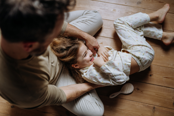 Top view of father with daughter on floor laughing together, having fun and tickling each other. Girls dad. Unconditional paternal love, Father's Day concept.