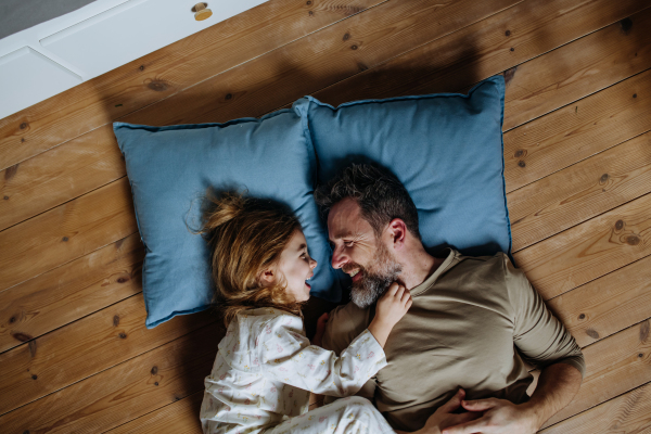 Top view of father with daughter lying on floor, pillows and laughing together. Girls dad. Unconditional paternal love, Father's Day concept.