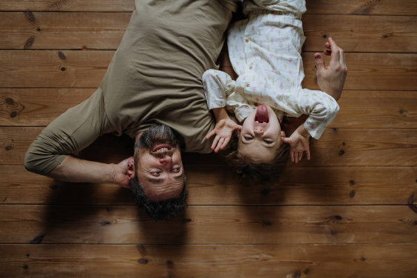 Top view of father with daughter lying on floor, making faces and laughing together. Girls dad. Unconditional paternal love, Father's Day concept.