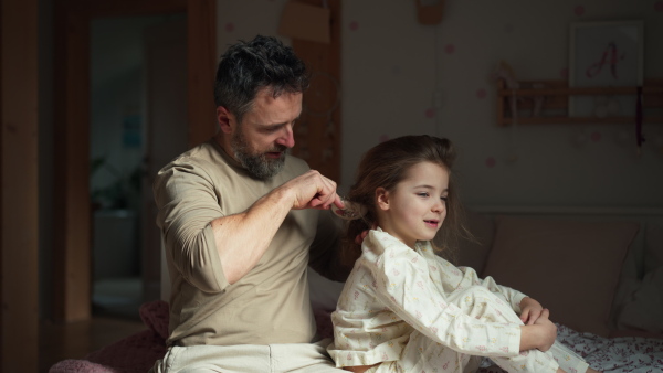 Father braiding his daughter's hair, combing hair as part of bedtime routine. Single dad taking care of his daughter's hairstyle.