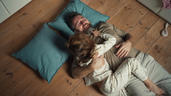 Top view of father with daughter lying on floor, making faces and laughing together. Girls dad. Unconditional paternal love, Father's Day concept.