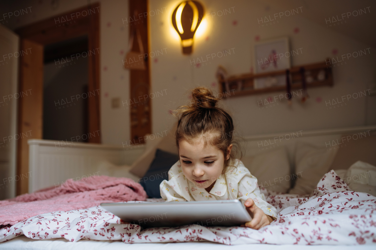 Cute girl lying on bed and watching something on tablet. Children's screen time.