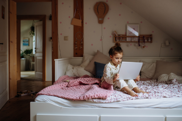 Cute girl sitting on bed and watching something on tablet. Children's screen time.