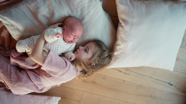 Portrait of big sister cuddling newborn, little baby. Girl lying with her new sibling in bed, closed eyes. Sisterly love, joy for the new family member.