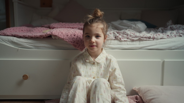 Cute girl sitting on floor in bedroom and looking at camera.. Children's free time.