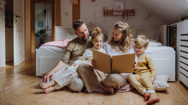 Beautiful family sitting in kids room on the floor, looking at old family photos in photoalbum. Calm hygge family moment.