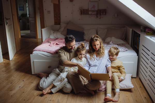 Beautiful family sitting in kids room on the floor, looking at old family photos in photoalbum. Calm hygge family moment.