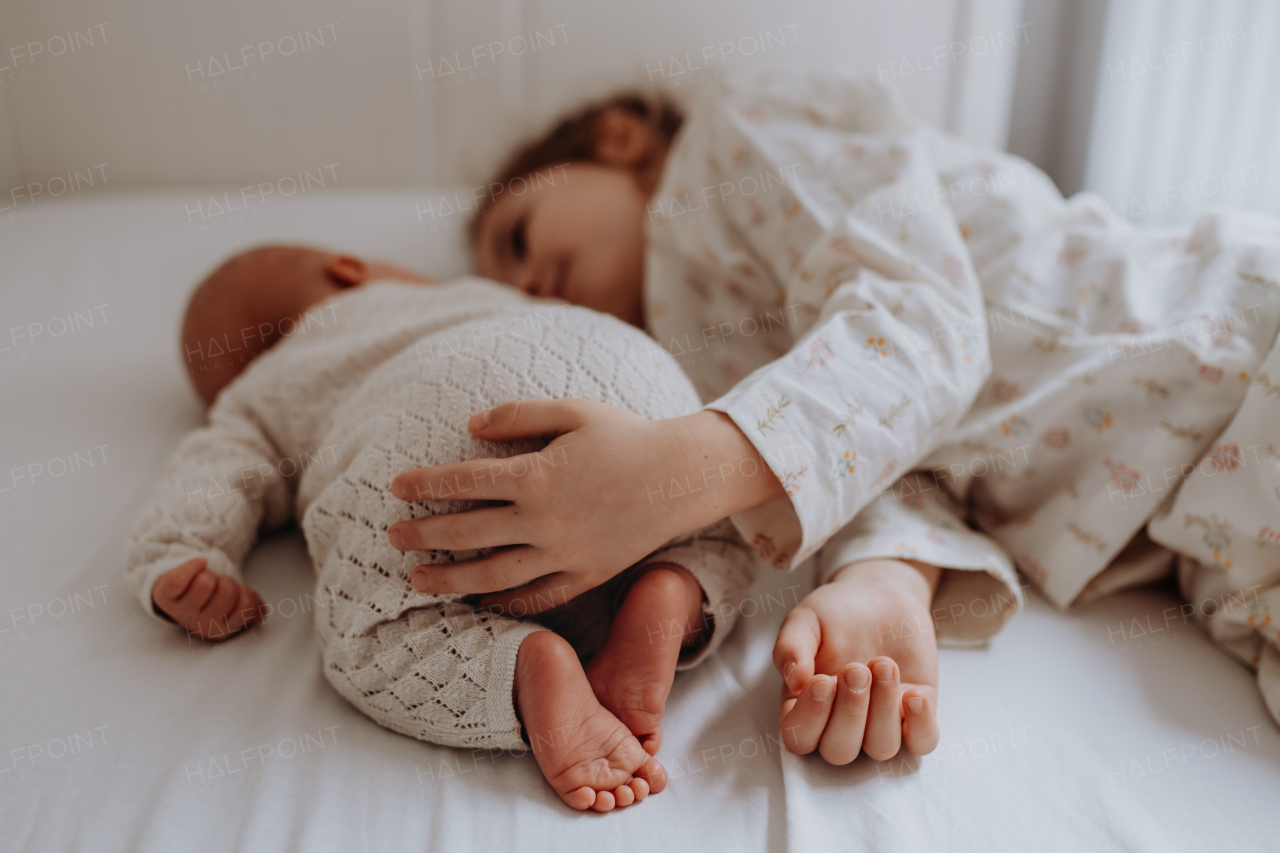 Portrait of big sister cuddling newborn, little baby. Girl lying with her new sibling in bed, closed eyes. Sisterly love, joy for the new family member.