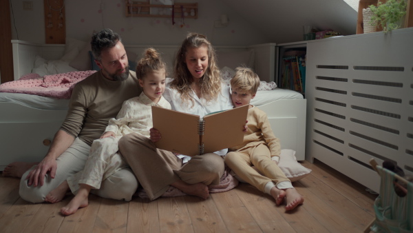 Beautiful family sitting in kids room on the floor, looking at old family photos in photoalbum. Calm hygge family moment.