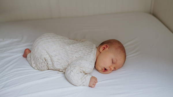 Portrait of cute little baby sleeping in bed, lying on on belly, closed eyes.