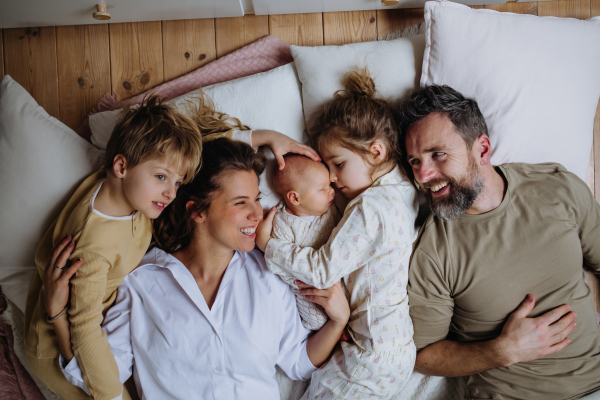 Top view of family lying in bed with kids and newborn baby. Perfect moment. Strong family, bonding, parents' unconditional love for their children.