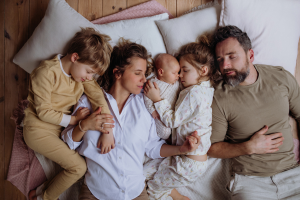 Top view of family sleeping in bed with kids and newborn baby. Perfect moment. Strong family, bonding, parents' unconditional love for their children.