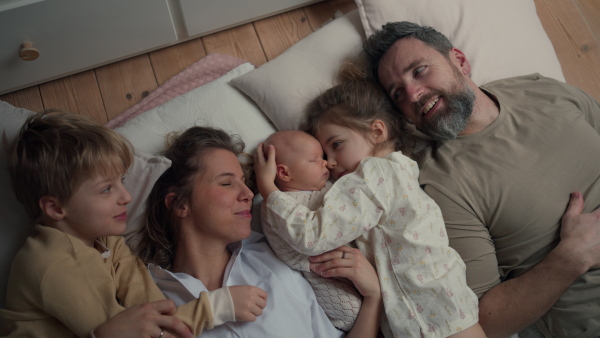 Top view of family lying in bed with kids and newborn baby. Perfect moment. Strong family, bonding, parents' unconditional love for their children.