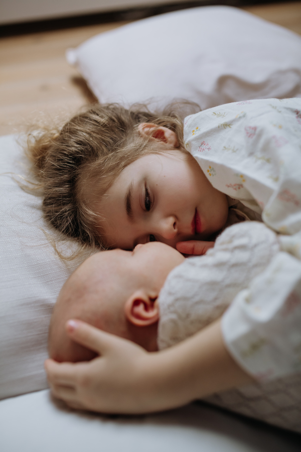 Portrait of big sister cuddling newborn, little baby. Girl lying with her new sibling in bed. Sisterly love, joy for the new family member.