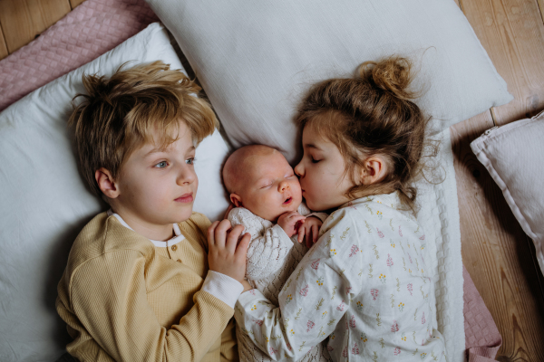 Portrait of big sister cuddling newborn, little baby. Girl lying with her new sibling in bed, closed eyes. Sisterly love, joy for the new family member.