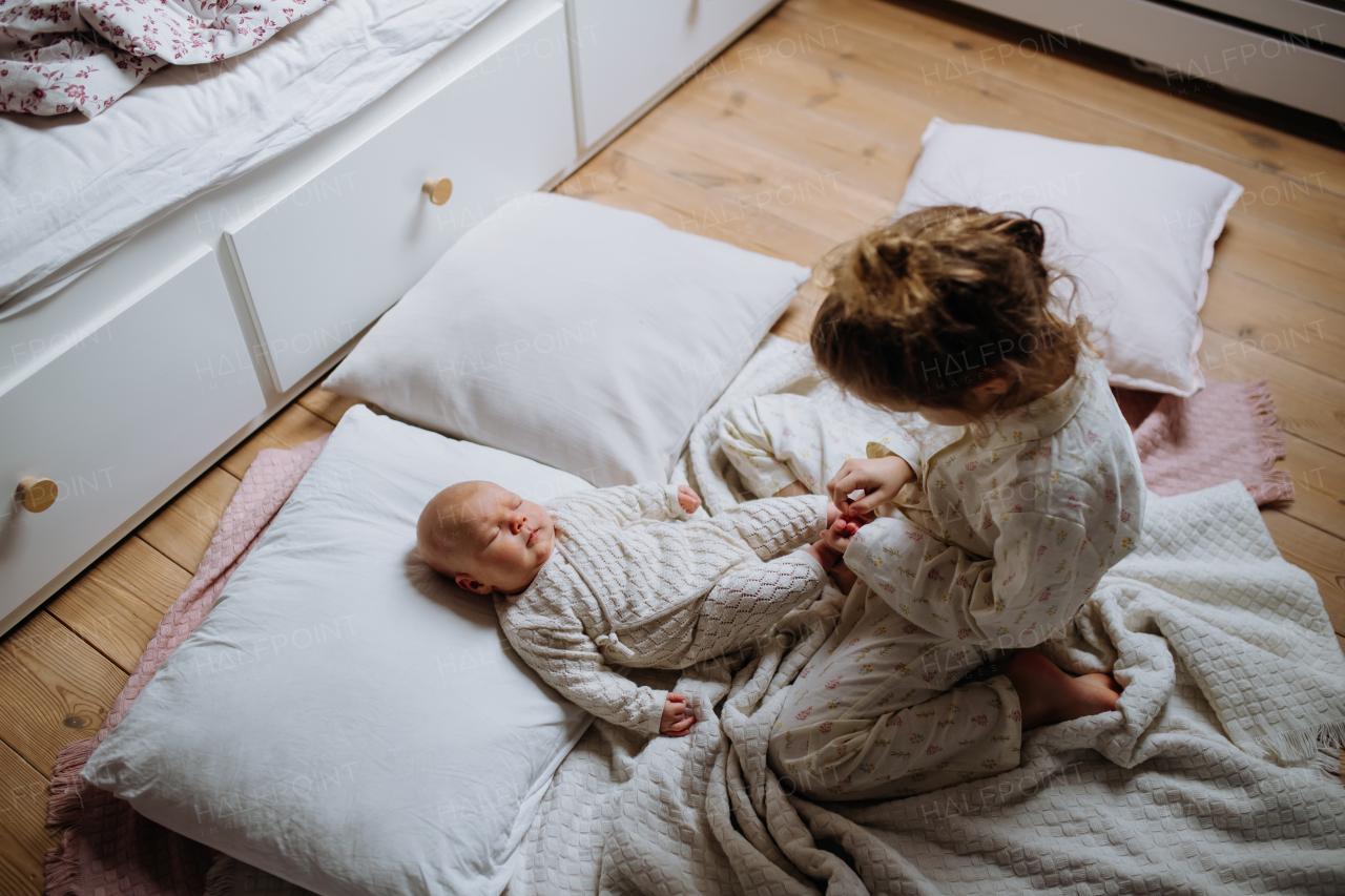 Big sister playing with newborn, little baby. Girl looking at sleeping new sibling, holding baby's small feet. Sisterly love, joy for new family member.