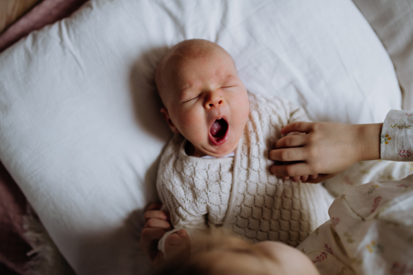 Top view of cute little baby yawning, sleeping in bed, big sister holding newborn hand. Sisterly love, joy for new family member.