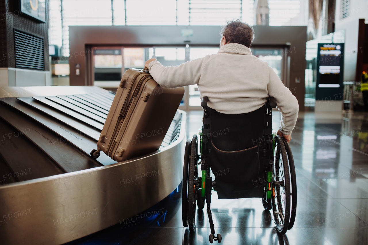 Rear view of a man on wheelchair at airport with his luggage.