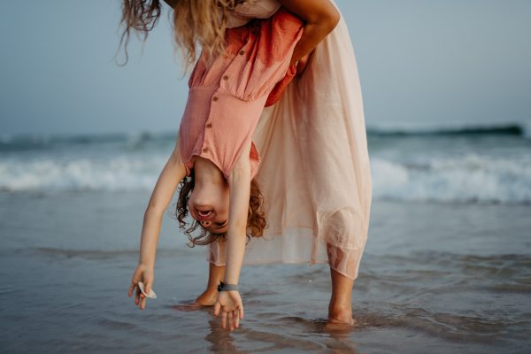 Mother holding her daughter upside down, enjoying summer vacation and having fun.