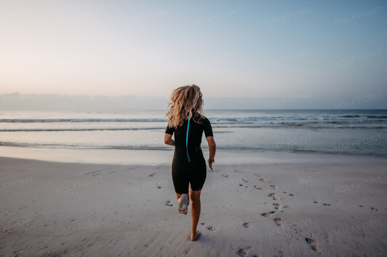 Rear view of woman in neoprene running in the ocean.