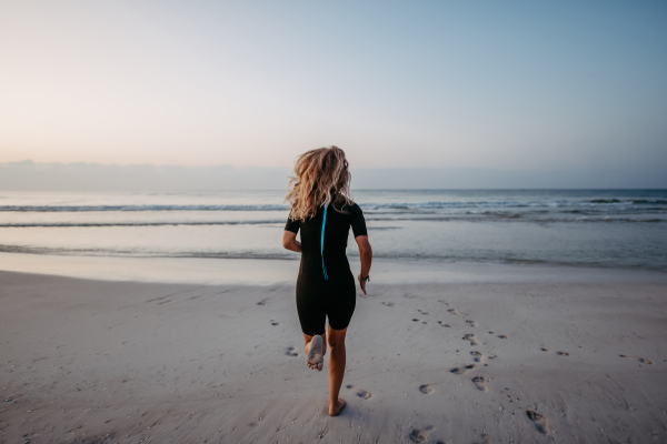 Rear view of woman in neoprene running in the ocean.