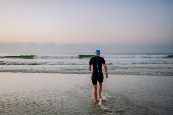 Rear view of woman in neoprene entering in the ocean.