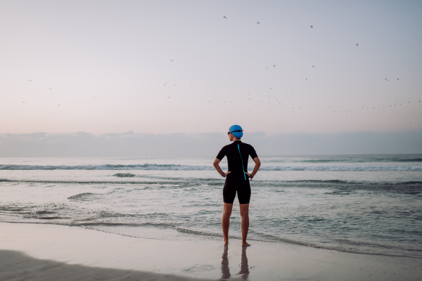 Rear view of woman in neoprene entering in the ocean.