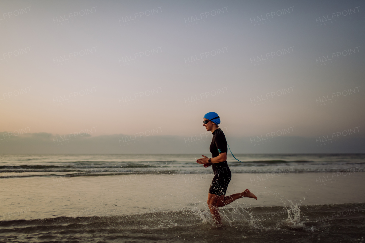 Side view of young woman in neoprene running in ocean.