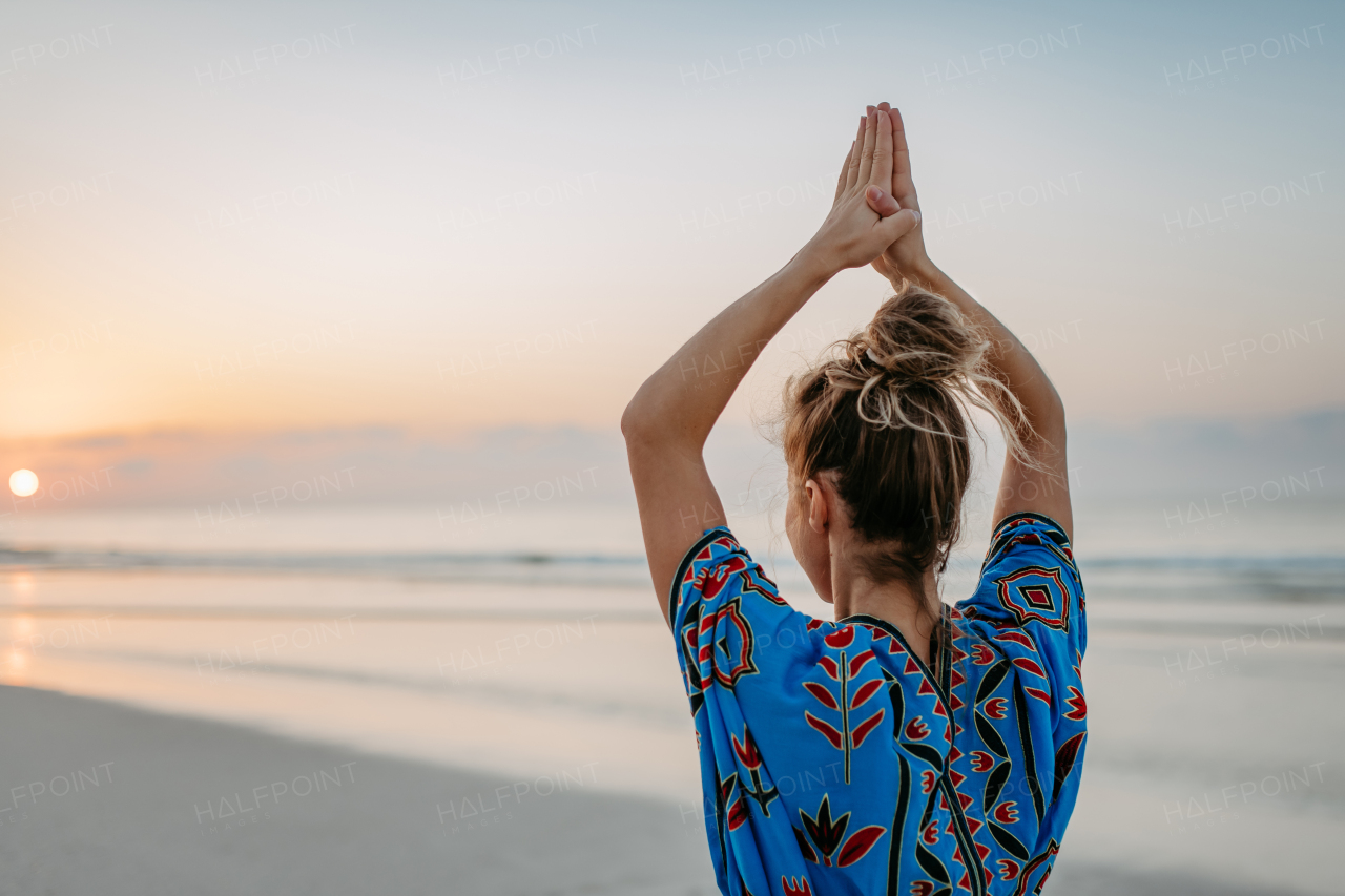 Rear view of young woman taking exercises at the beach, morning routine and healthy lifestyle concept.