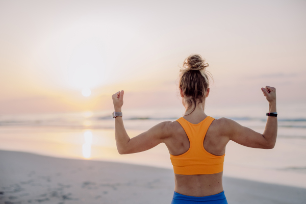 Rear view of young woman taking exercises at the beach, morning routine and healthy lifestyle concept.