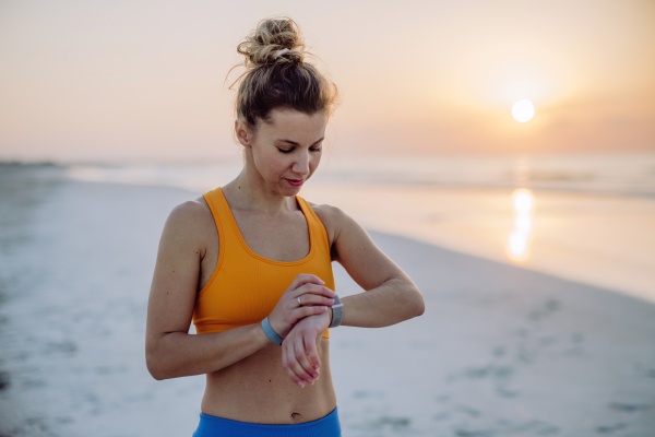 Young woman taking exercises at beach and checking the smartwatch, morning routine and healthy lifestyle concept.