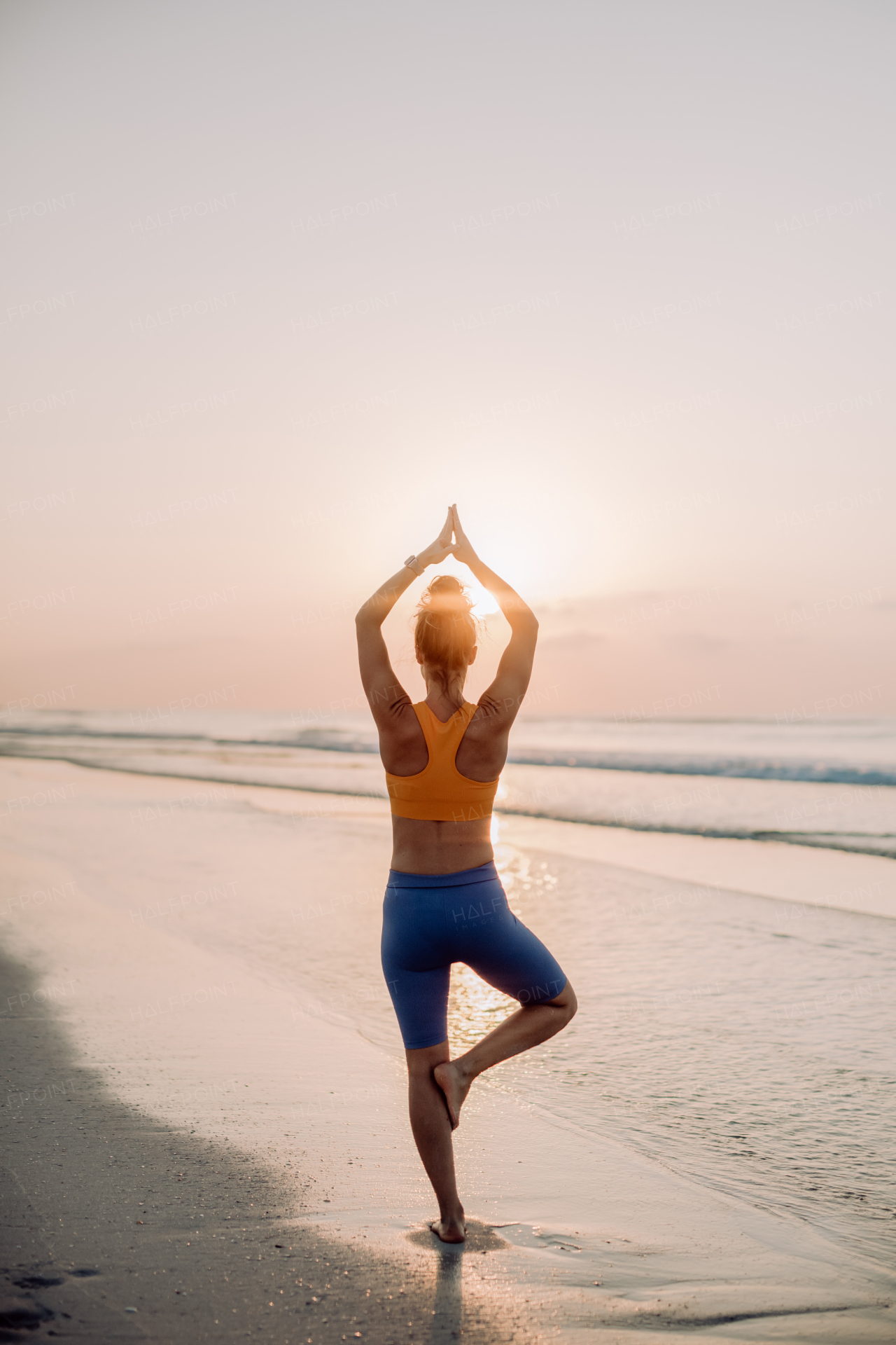 Rear view of young woman taking exercises at the beach, morning routine and healthy lifestyle concept.