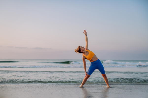 Young woman taking exercises at the beach, morning routine and healthy lifestyle concept.