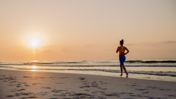 Rear view of young woman running at the beach, morning routine and healthy lifestyle concept.