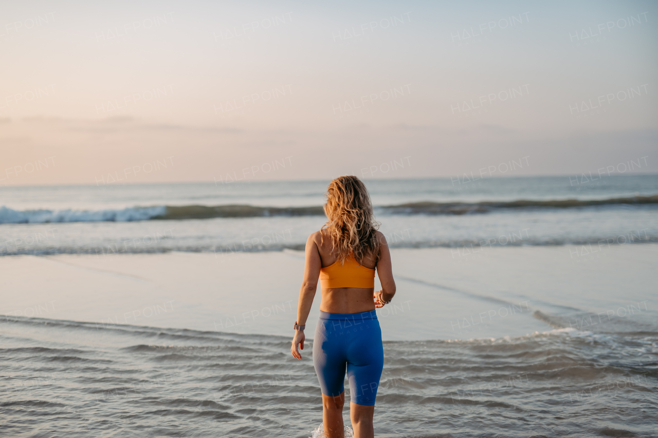 Rear view of young woman running on the beach, morning routine and healthy lifestyle concept.