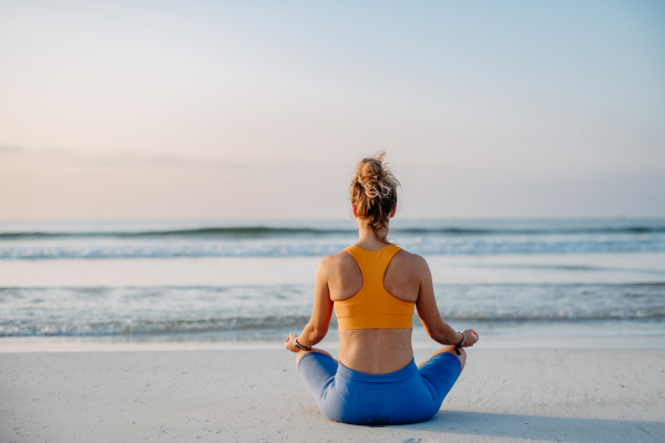 Rear view of young woman taking exercises at the beach, morning routine and healthy lifestyle concept.