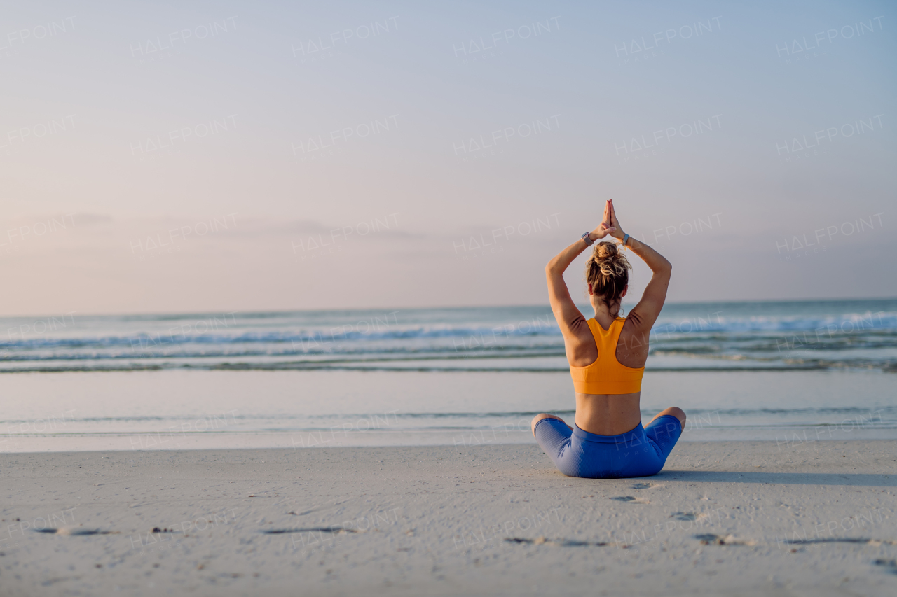 Rear view of young woman taking exercises at the beach, morning routine and healthy lifestyle concept.