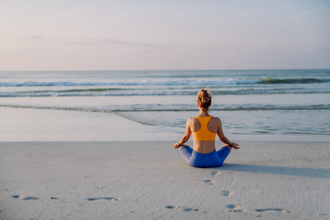 Rear view of young woman taking exercises at the beach, morning routine and healthy lifestyle concept.