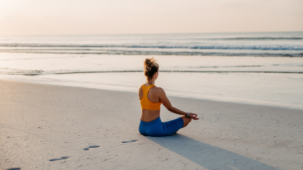 Rear view of young woman taking exercises at the beach, morning routine and healthy lifestyle concept.