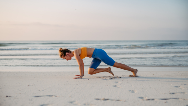 Young woman taking exercises at the beach, morning routine and healthy lifestyle concept.